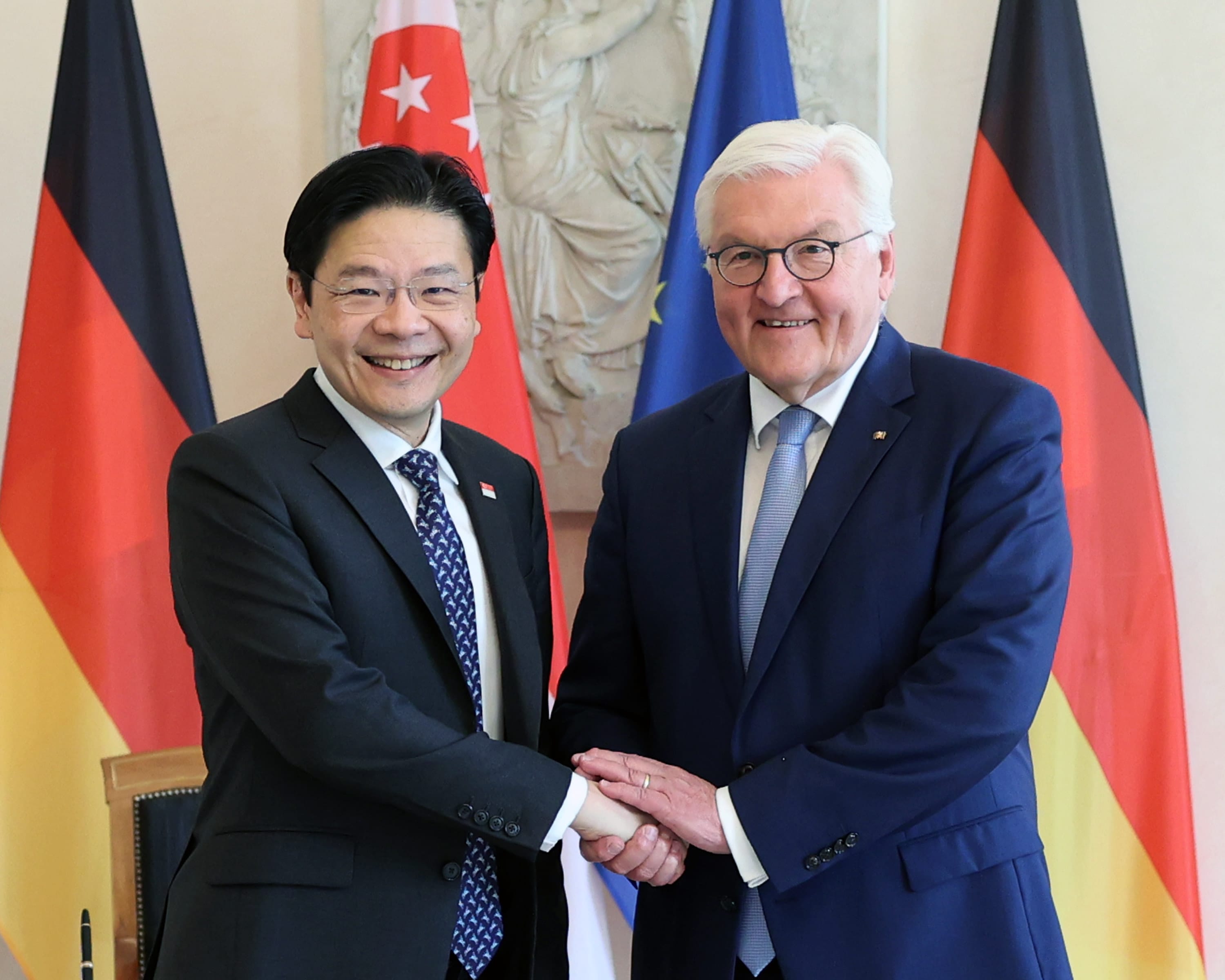 Two men in suits shake hands; Singapore and Germany flags are in the background.